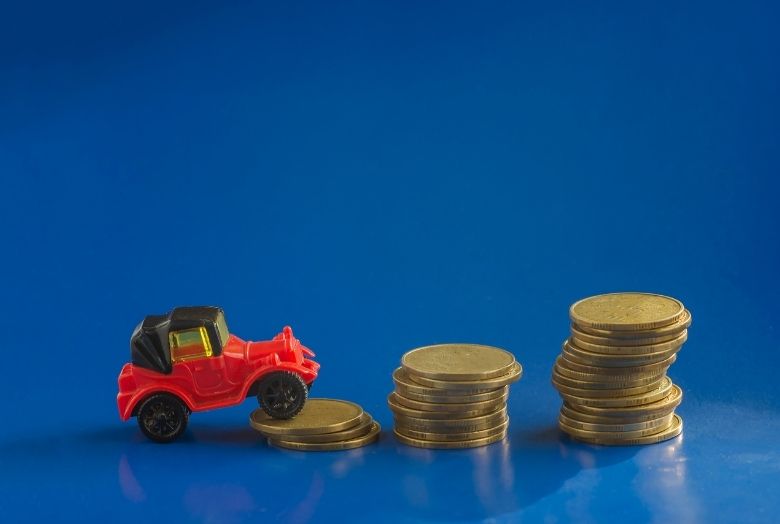 carro em miniatura subindo uma montanha de moedas empilhadas com fundo azul