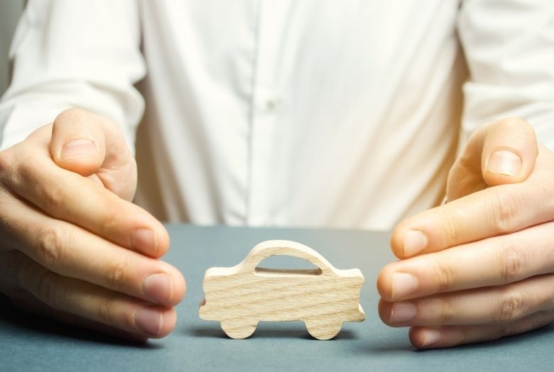 duas mãos formando uma cerca de proteção ao redor de um carro em miniatura