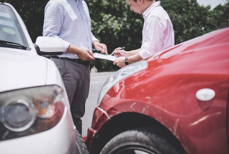 Dois homens preenchendo uma prancheta de seguro após um acidente entre dois carros