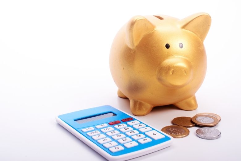 Cofre de porquinho douradoao lado de uma calculadora e algumas moedas