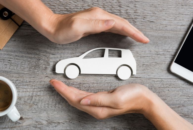 um par de mãos protegendo um carro branco em miniatura