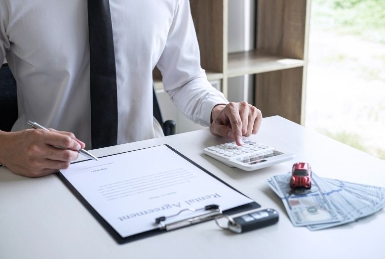 Homem fazendo contas em uma calculado e assinando um contrato