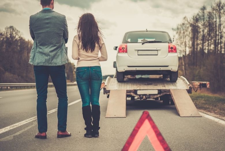 Um casal de costas olhando um carro ser levado pelo guincho.