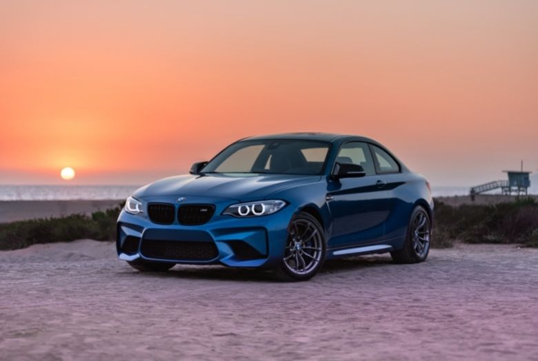 carro azul com por do sol no horizonte ao fundo.