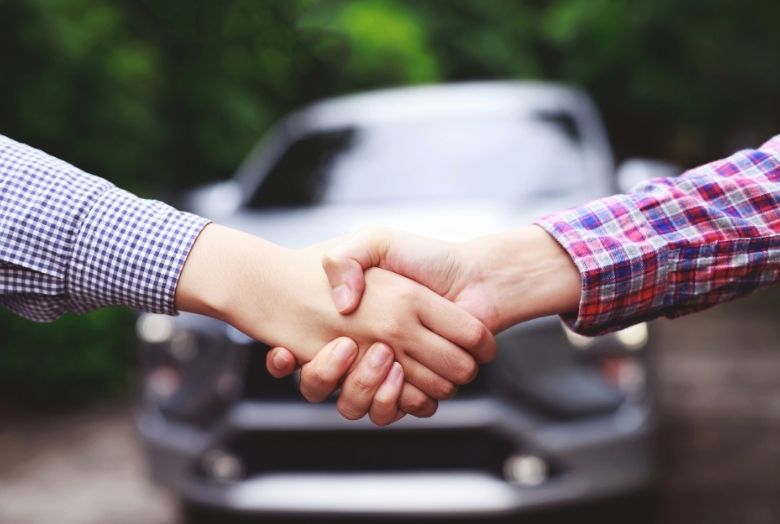 duas pessoas apertando as mãos com um carro desfocado ao fundo