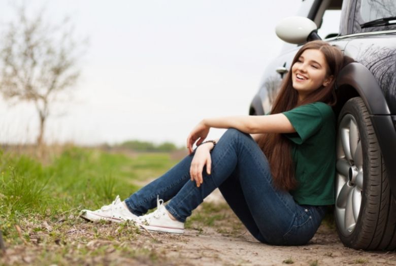 Mulher sentada no chão encostada em um carro sorrindo